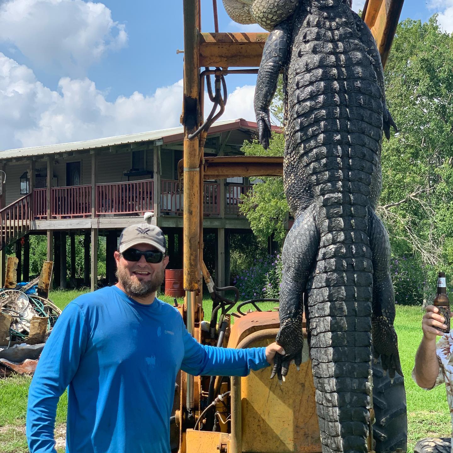 Man shown with large gator being held up by a tractor in Louisiana.